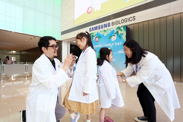 임직원 자녀들이 엄마아빠와 함께 실험실 가운입기 체험을 하고 있는 모습&lt;삼성바이오로직스&gt;<br>
